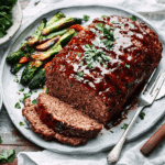 A sliced spicy meatloaf topped with tangy glaze served with mashed potatoes.