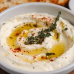 Whipped ricotta dip in a bowl topped with olive oil and herbs.